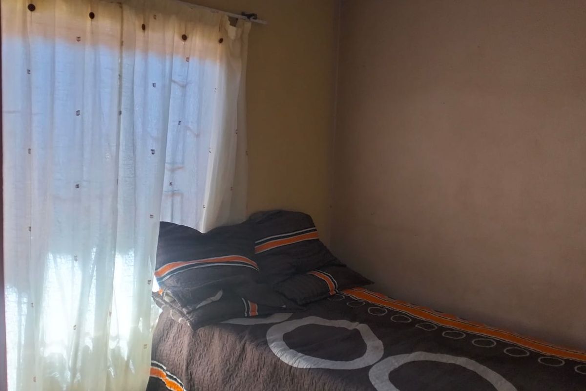 A compact bedroom featuring a window with a curtain rail and plain wall finishes.