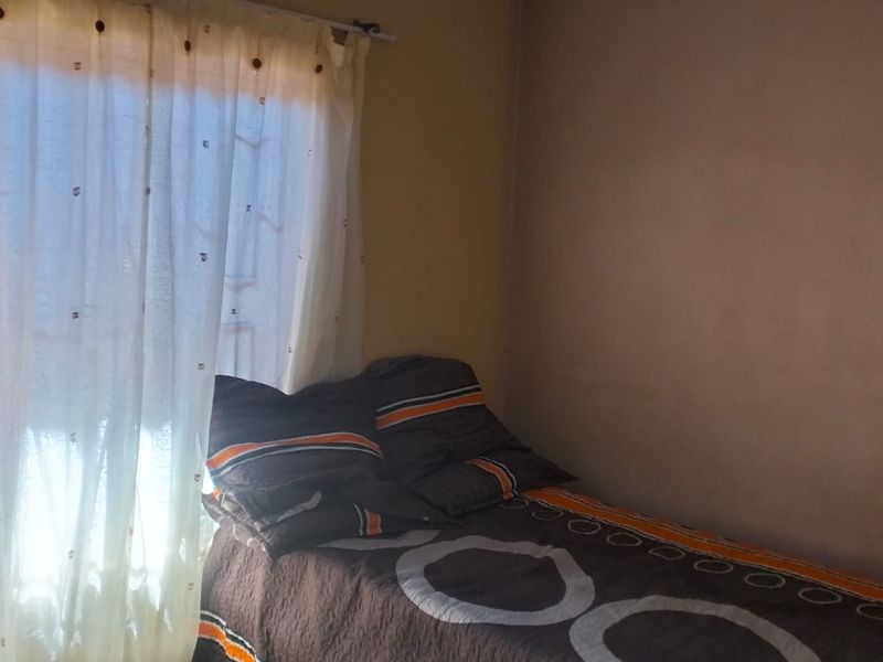 A compact bedroom featuring a window with a curtain rail and plain wall finishes.