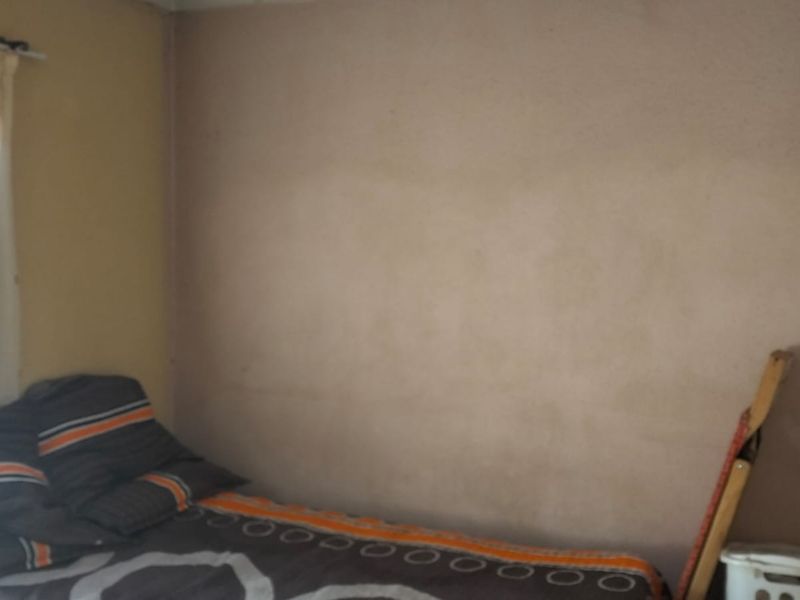 A simple bedroom featuring plain walls and a window with a curtain rod.