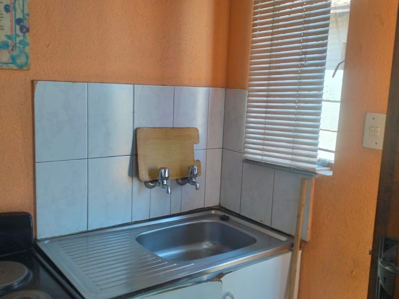 A compact kitchen area featuring a stainless steel sink, tiled splashback, and built-in stove, requiring cosmetic updates to improve the overall aesthetic.