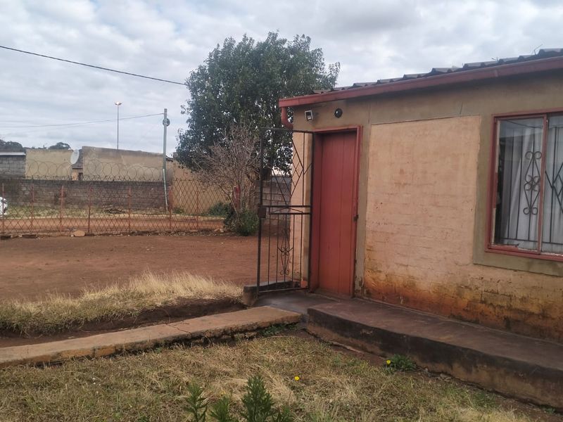 Front exterior view of the property featuring a simple facade, security gate, and a basic concrete pathway leading to the entrance.