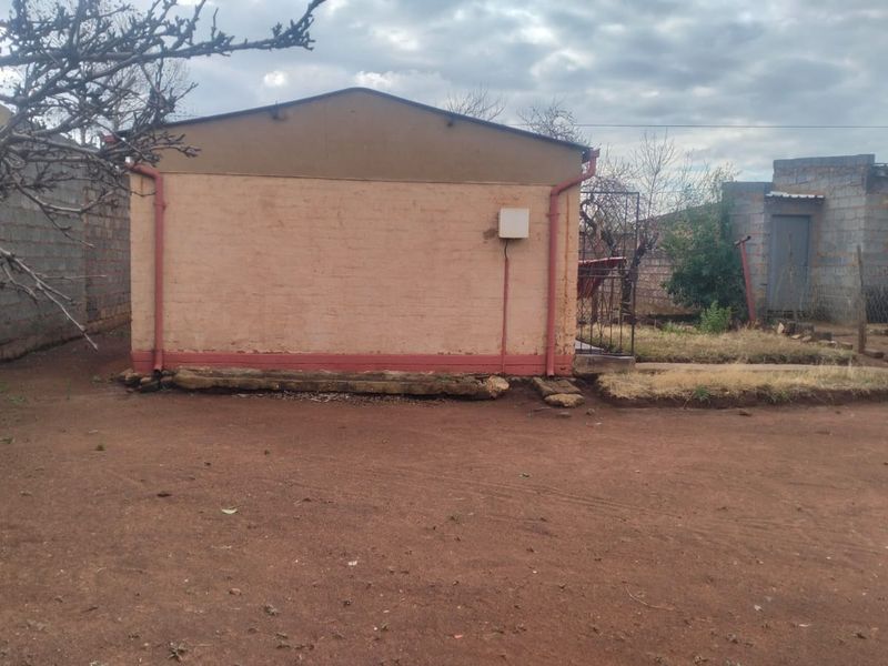 Rear view of the property showing a simple brick structure with basic exterior finishes and an unpaved yard area.