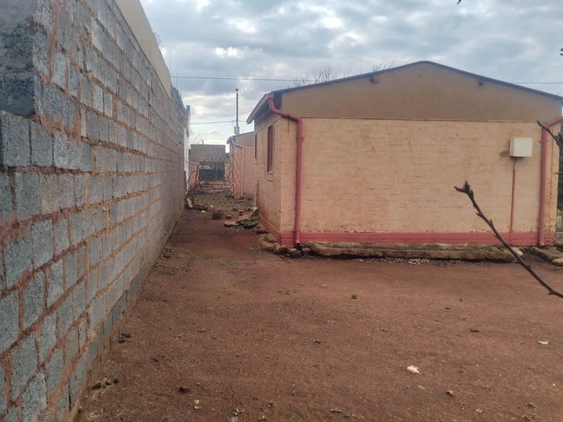 Rear exterior view of the property showing a cinder block boundary wall and basic brick structure with unpaved ground.