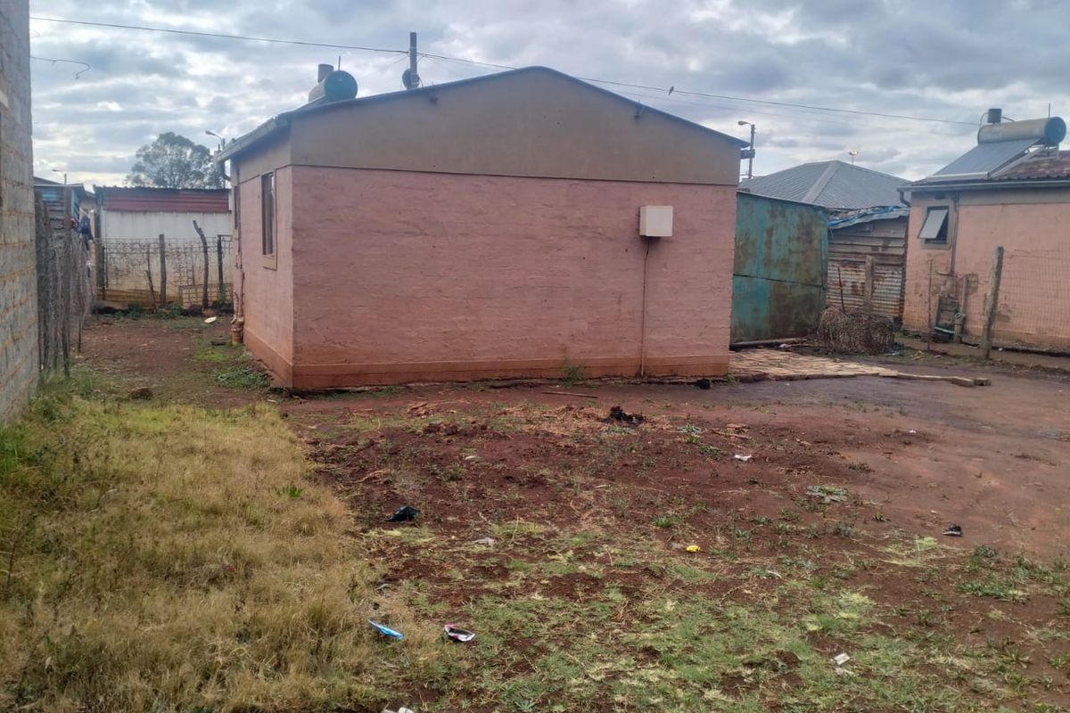 Rear exterior view of the property showing the building structure, solar water heater, and surrounding yard area with basic fencing.