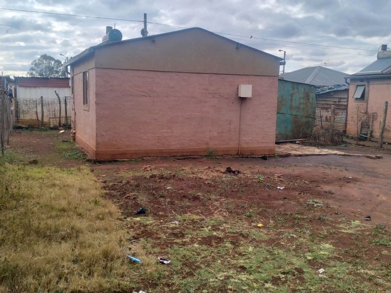 Rear exterior view of the property showing the building structure, solar water heater, and surrounding yard area with basic fencing.