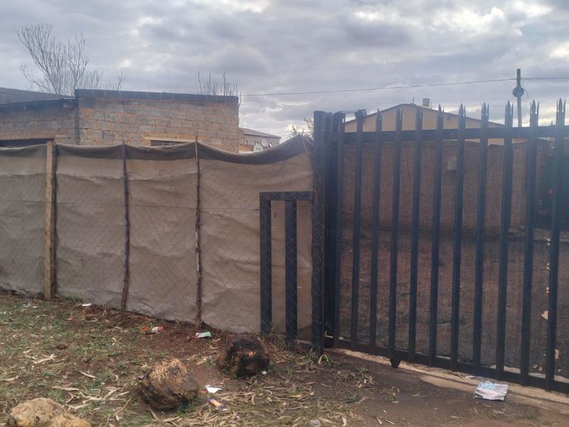 Front exterior view showing a metal security gate and perimeter fencing with shade cloth screening.