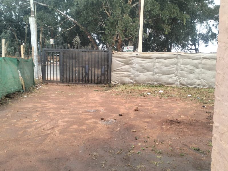 An unpaved front yard area featuring a metal gate and basic perimeter fencing, requiring significant landscaping and surface improvements.