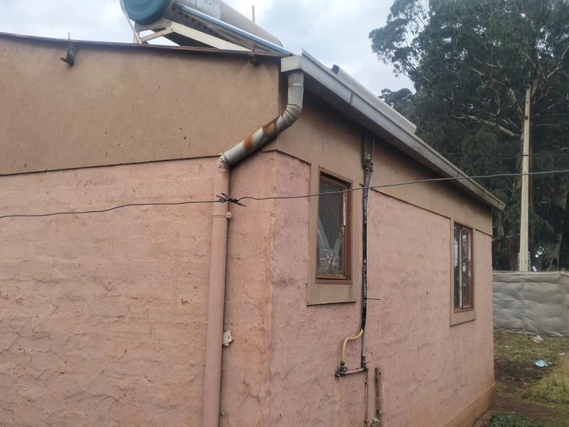 Rear exterior view of the property showing weathered wall finishes, a solar water heater installation, and visible wear on external plumbing and window frames.