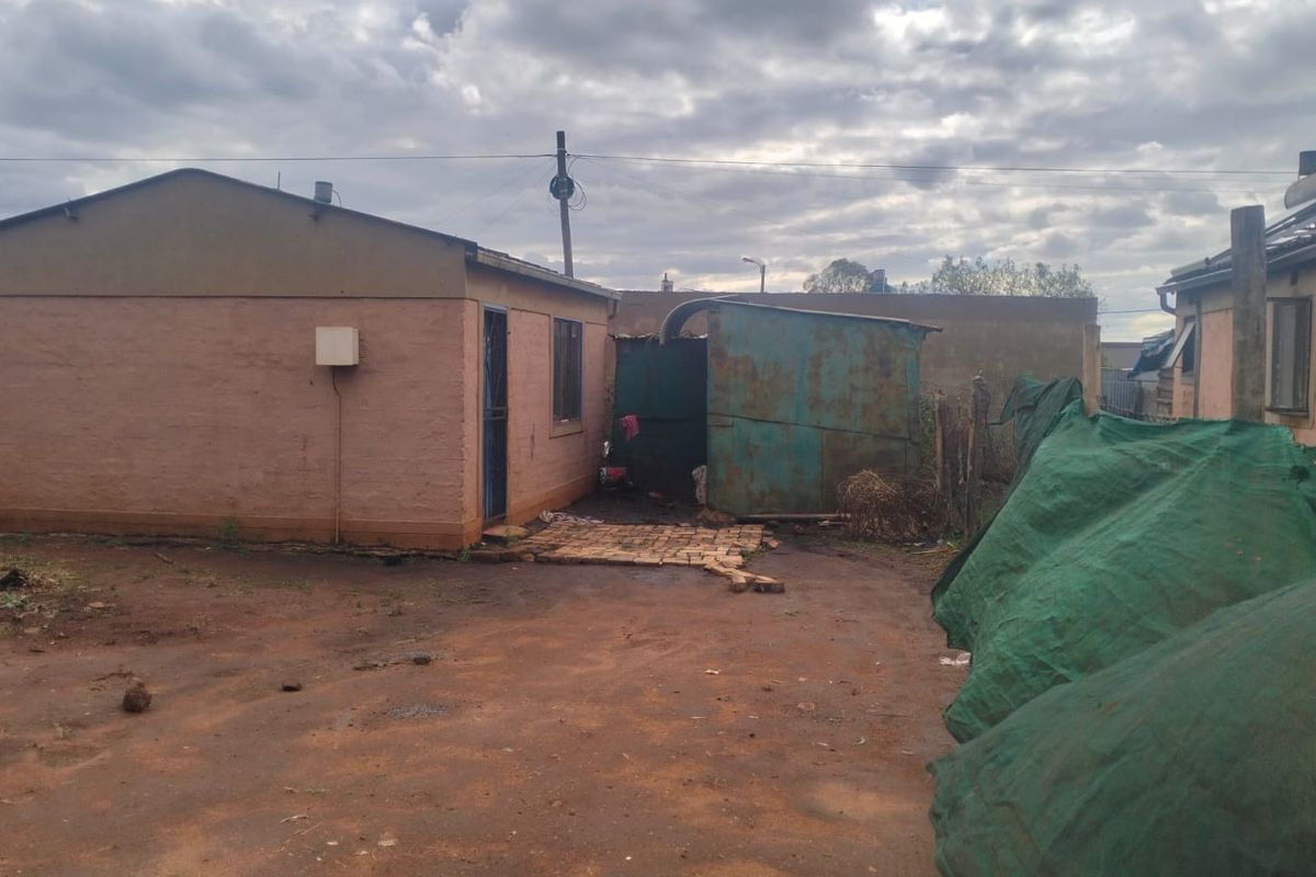 Rear view of the property showing a basic structure with a solar water heater and an adjacent metal shed on a dirt yard.