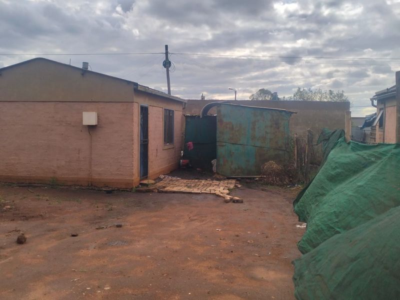 Rear view of the property showing a basic structure with a solar water heater and an adjacent metal shed on a dirt yard.