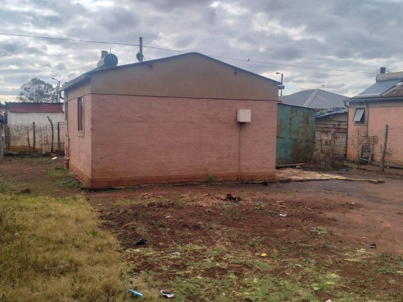 Rear view of the property showing exterior masonry walls, solar water heating infrastructure, and surrounding yard space with basic fencing.