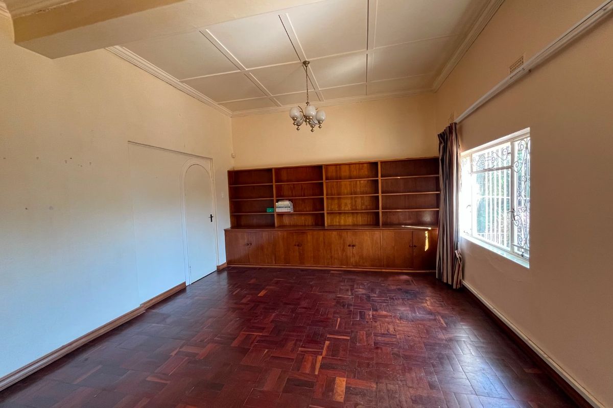 Spacious living room featuring original parquet flooring, a large built-in wooden bookshelf, and classic ceiling molding, offering a versatile space for living or study.