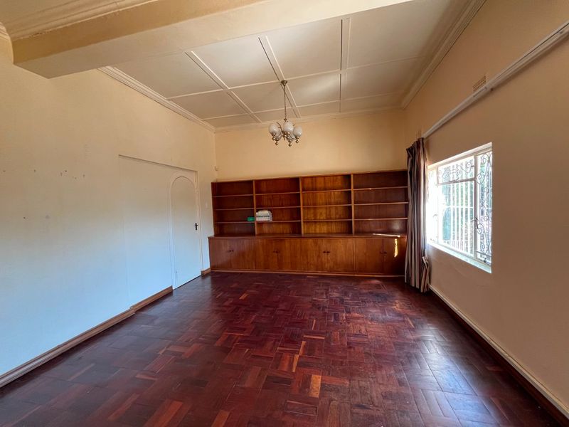 Spacious living room featuring original parquet flooring, a large built-in wooden bookshelf, and classic ceiling molding, offering a versatile space for living or study.