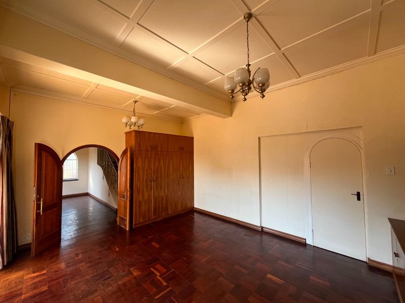 Spacious bedroom featuring original parquet flooring, built-in wooden cupboards, a decorative coffered ceiling, and an arched doorway leading to an adjacent hallway.