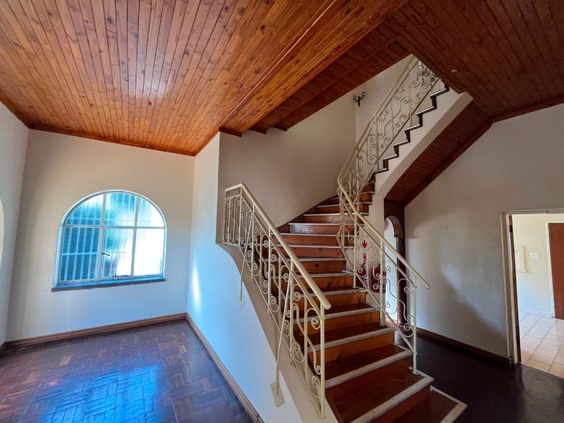 Spacious entrance hall featuring a timber staircase with wrought iron balustrade, parquet flooring, and a distinctive arched window with security bars.