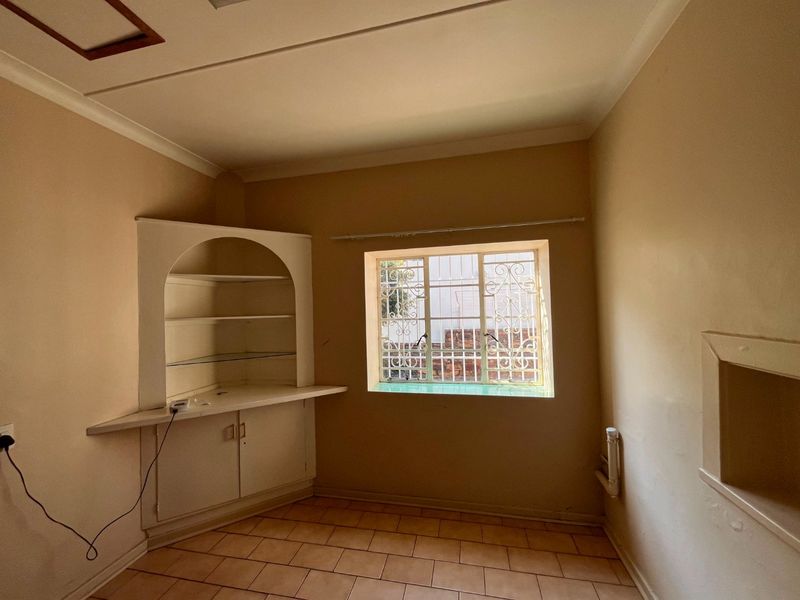An empty bedroom featuring tiled flooring, a built-in arched shelving unit with lower cabinetry, and a window fitted with security bars.