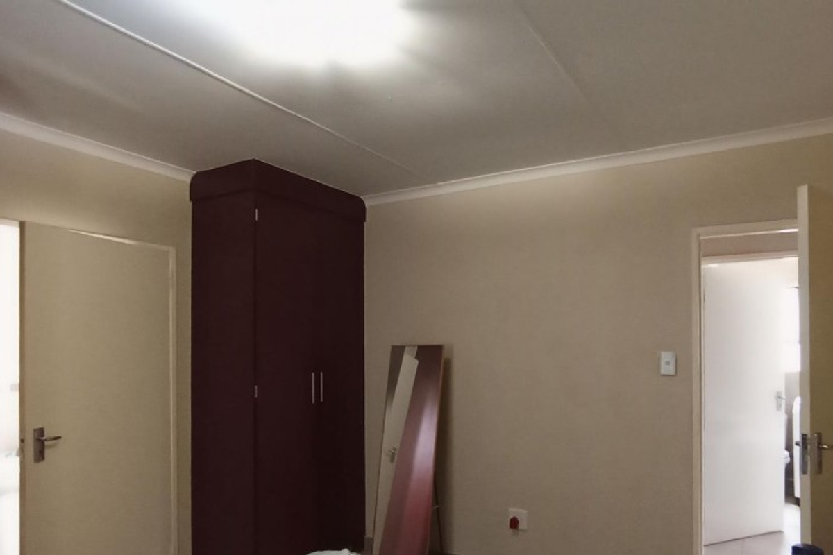 A neutral bedroom featuring built-in dark wood cupboards, coving, and access to adjacent rooms.