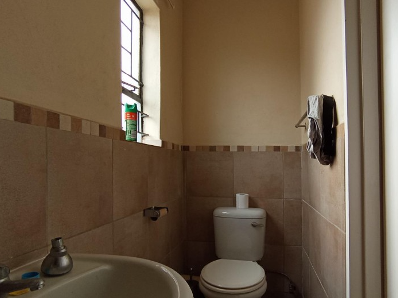 A compact bathroom featuring a pedestal basin, toilet, and neutral wall tiling with a decorative border.
