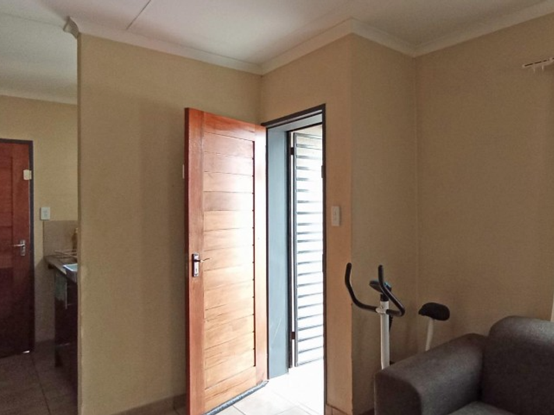 A living area featuring tiled flooring, neutral wall tones, and wooden doors leading to adjacent spaces.