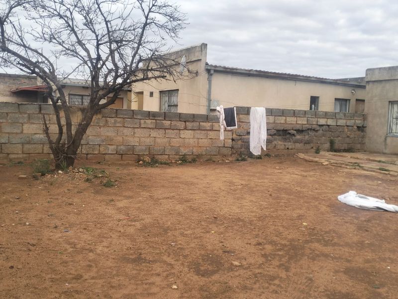 A rear exterior view of the property featuring a large unpaved yard area enclosed by a concrete block boundary wall.