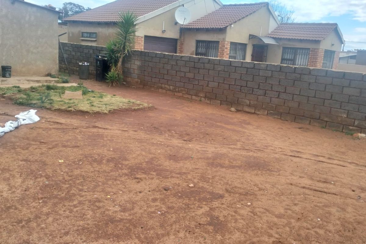Rear view of the property featuring a large unpaved yard area enclosed by a concrete block boundary wall.