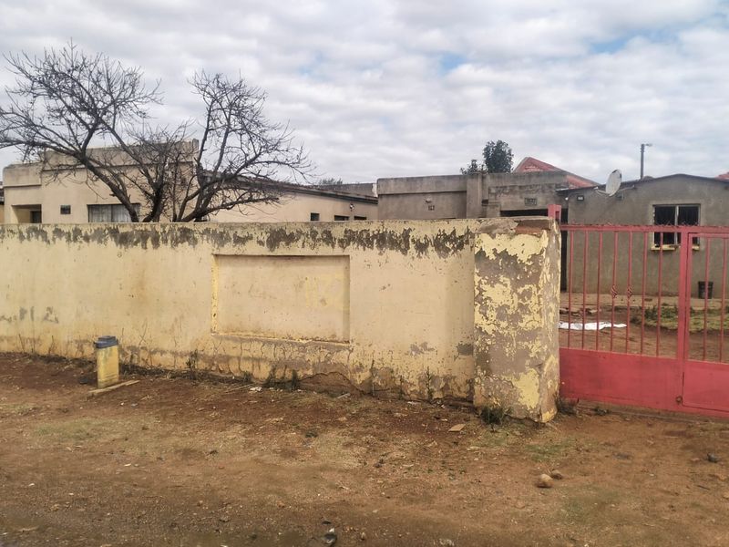 Front view of the property featuring a weathered perimeter wall and a metal entrance gate, showing significant signs of exterior wear.