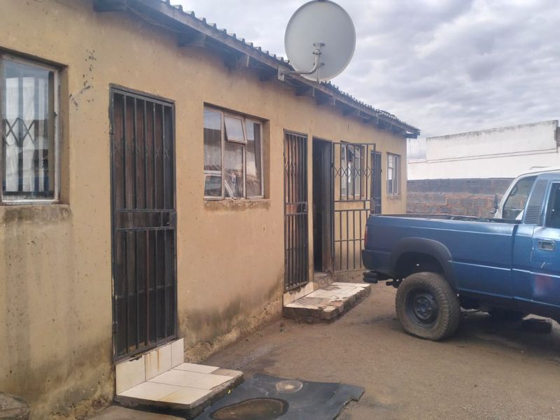Rear exterior view of the property featuring security gates, metal window frames, and satellite dish installation on a weathered plaster wall finish.