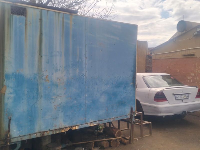 A rear yard area featuring a weathered, blue metal storage structure and paved ground surface.