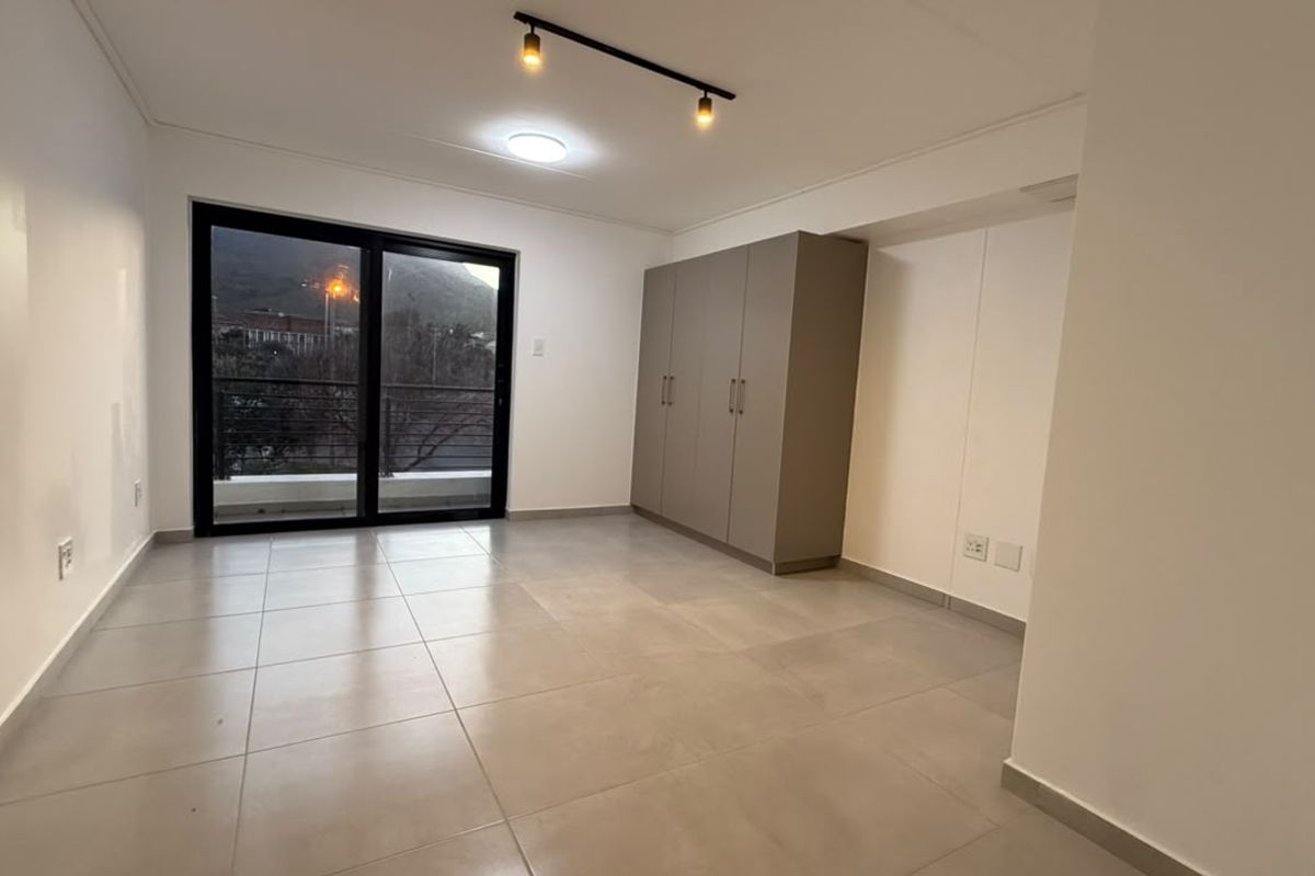 A bright, empty bedroom featuring neutral tiled flooring, built-in cupboards, and a sliding glass door leading to an outdoor balcony.