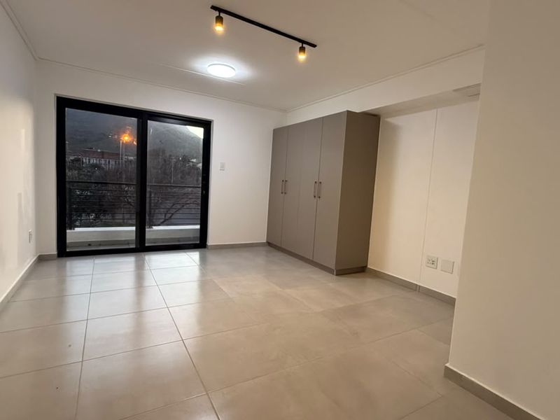 A bright, empty bedroom featuring neutral tiled flooring, built-in cupboards, and a sliding glass door leading to an outdoor balcony.