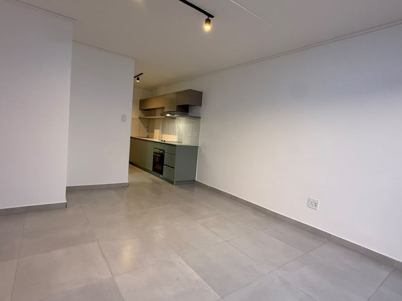 An open-plan living area featuring modern tiled flooring, track lighting, and a compact kitchen with built-in cabinetry, oven, and extractor fan.