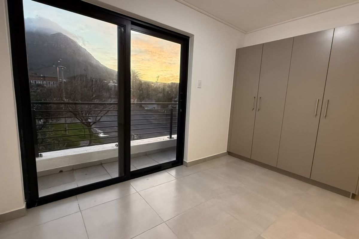 A bright, empty bedroom featuring modern built-in cupboards, large sliding glass doors, and direct access to a private balcony with scenic views.