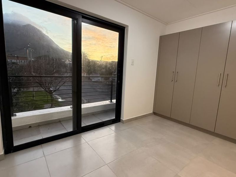 A bright, empty bedroom featuring modern built-in cupboards, large sliding glass doors, and direct access to a private balcony with scenic views.