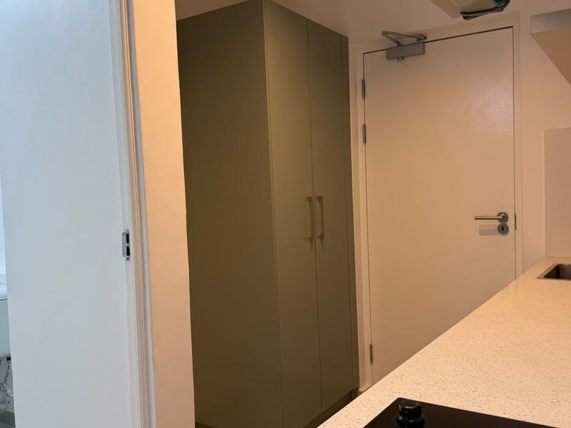 An open-plan apartment interior featuring a compact kitchen with stone countertops, built-in cabinetry, and an adjacent bathroom with a modern toilet.