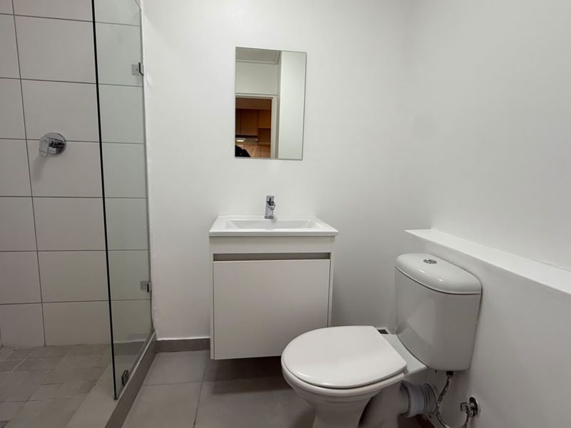 A clean, modern bathroom featuring a glass-enclosed shower, a wall-mounted vanity with basin, and a standard toilet.