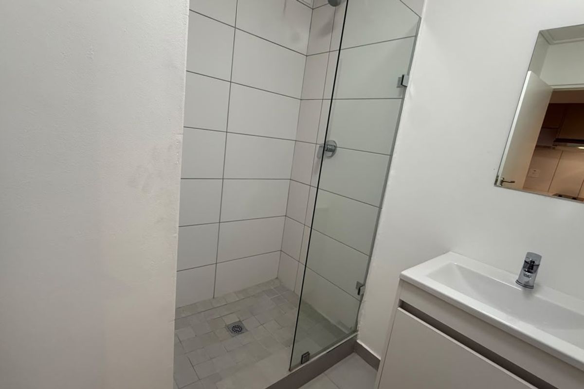 A clean, modern bathroom featuring a glass-enclosed shower with white wall tiles and a sleek vanity unit with a wall-mounted mirror.