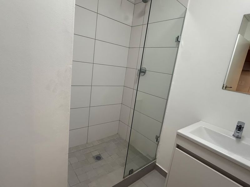 A clean, modern bathroom featuring a glass-enclosed shower with white wall tiles and a sleek vanity unit with a wall-mounted mirror.