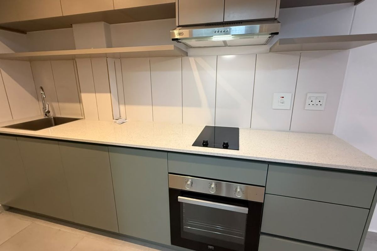 Modern kitchen featuring sage green cabinetry, stone countertops, integrated oven, electric hob, and a stainless steel sink with a tiled splashback.