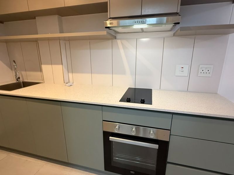 Modern kitchen featuring sage green cabinetry, stone countertops, integrated oven, electric hob, and a stainless steel sink with a tiled splashback.