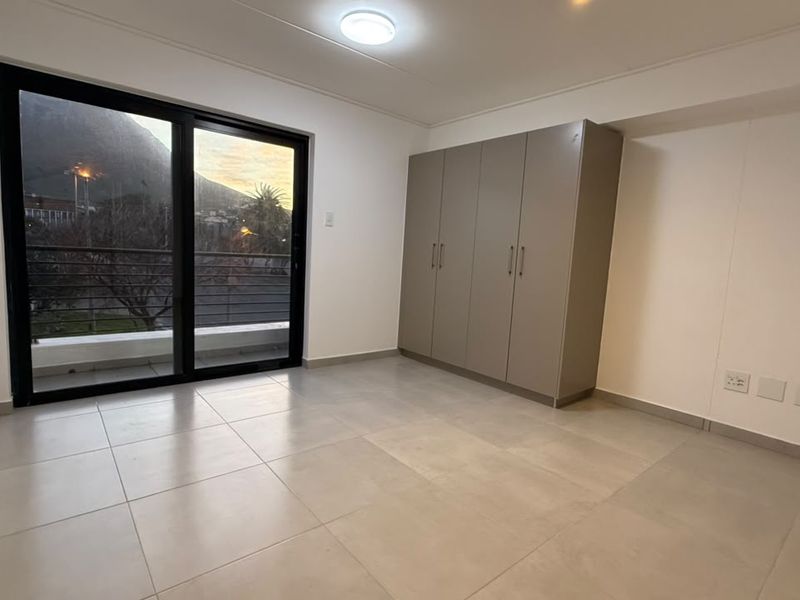 A bright, empty bedroom featuring large sliding glass doors leading to a balcony, neutral tiled flooring, and a modern built-in wardrobe.