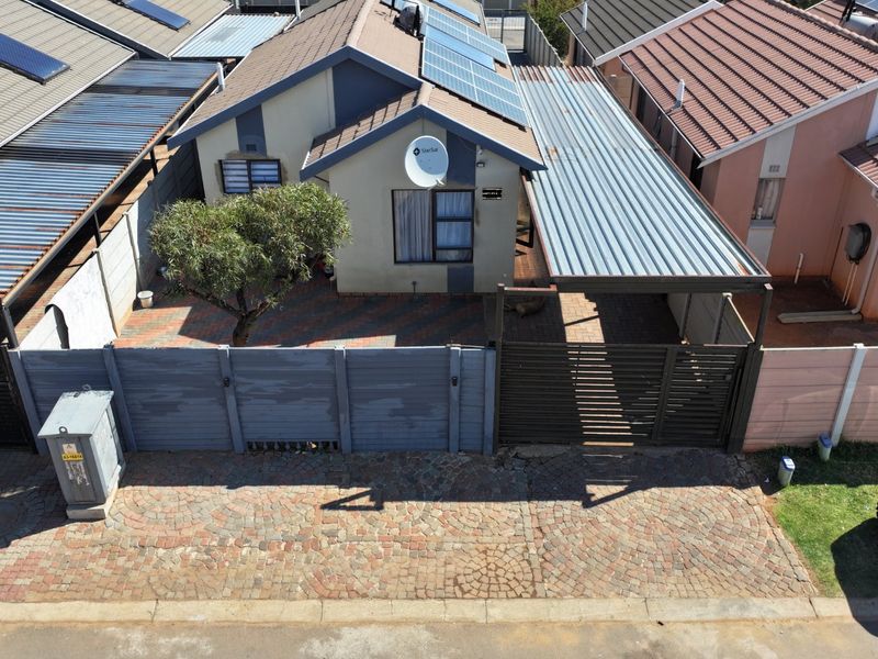 Aerial view of a residential property featuring a paved driveway, carport, solar panels, and a secure boundary wall.
