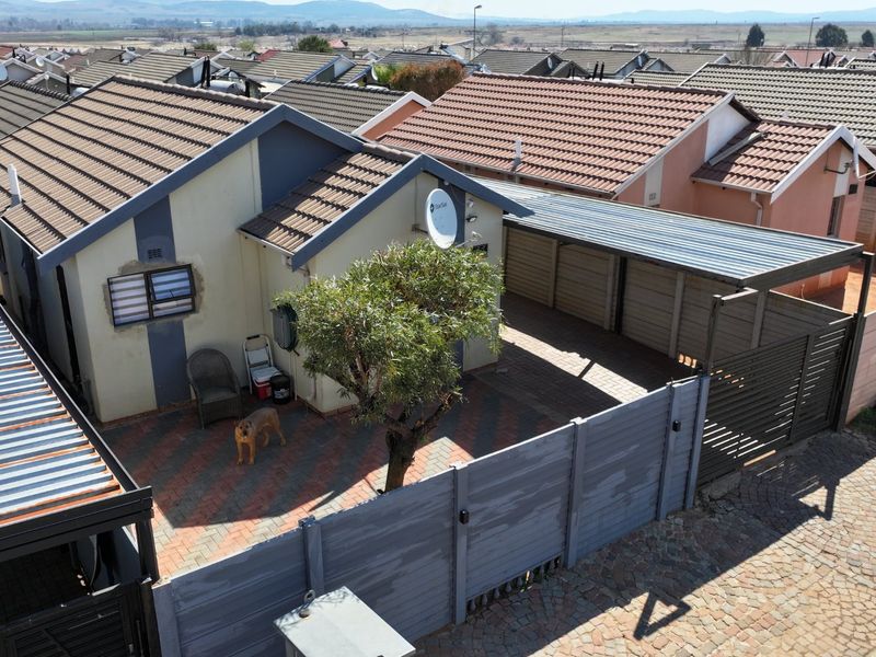 Aerial view of a residential property featuring a paved driveway, carport, and tiled roof, situated within a suburban housing development.