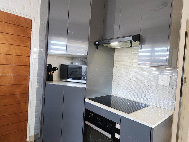 Modern kitchen featuring sleek grey cabinetry, stone countertops, built-in oven, electric hob, and a stylish tiled backsplash.