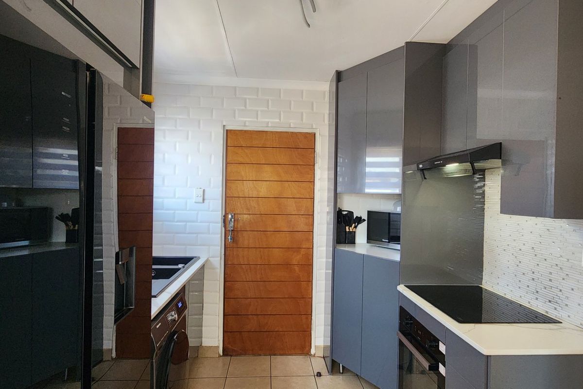 Modern kitchen featuring sleek grey cabinetry, subway tile backsplash, integrated electric hob, oven, and extractor fan with tiled flooring.