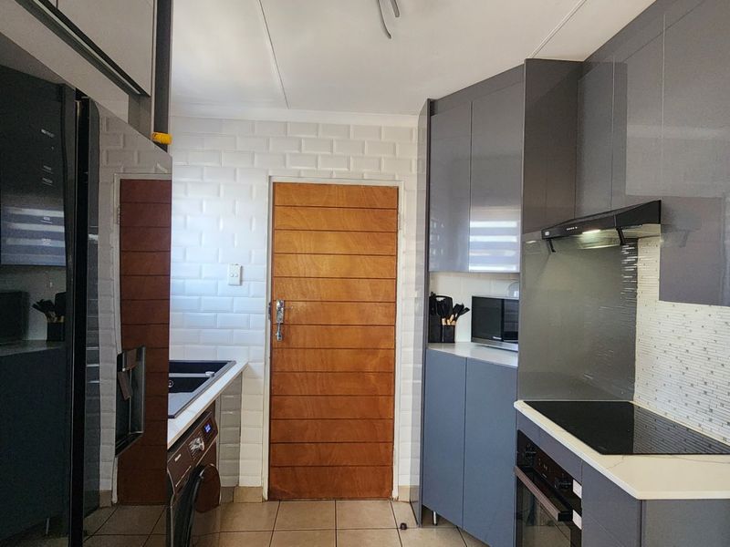 Modern kitchen featuring sleek grey cabinetry, subway tile backsplash, integrated electric hob, oven, and extractor fan with tiled flooring.