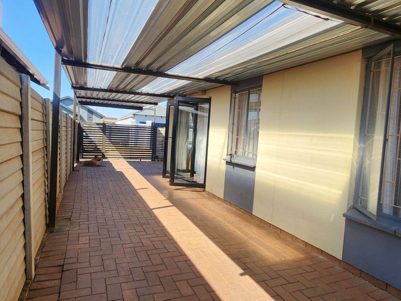 A covered outdoor patio area featuring paved flooring, a corrugated metal roof, and secure access to the interior through double glass doors.