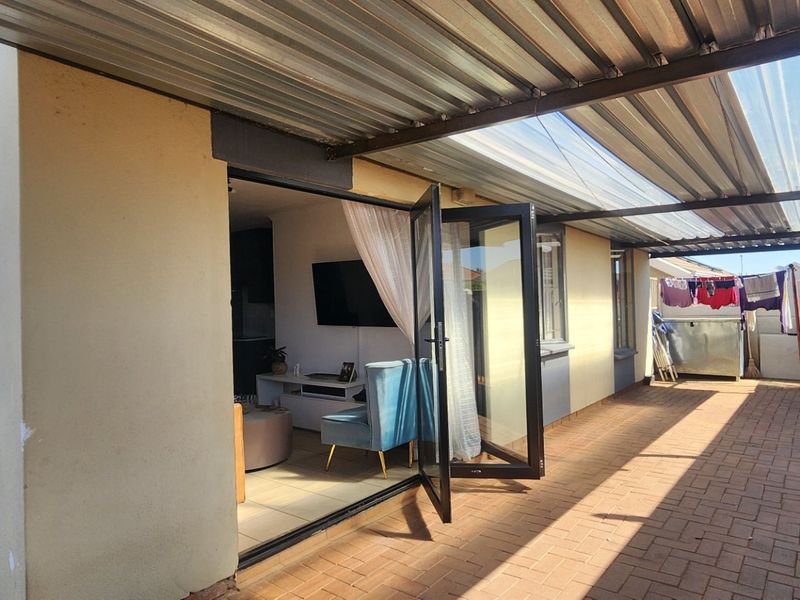 A covered paved patio area featuring a corrugated metal roof, bi-fold doors leading into the home, and a secure precast concrete boundary wall.