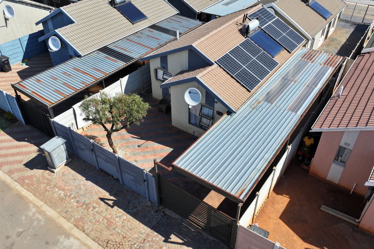 Aerial view of a residential property featuring a tiled roof with solar panels, a paved courtyard, and a covered carport area.