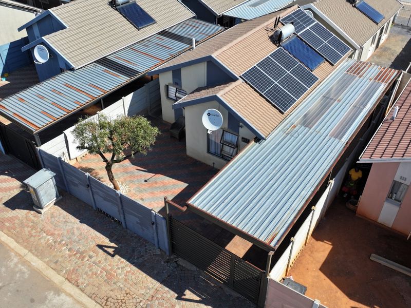 Aerial view of a residential property featuring a tiled roof with solar panels, a paved courtyard, and a covered carport area.