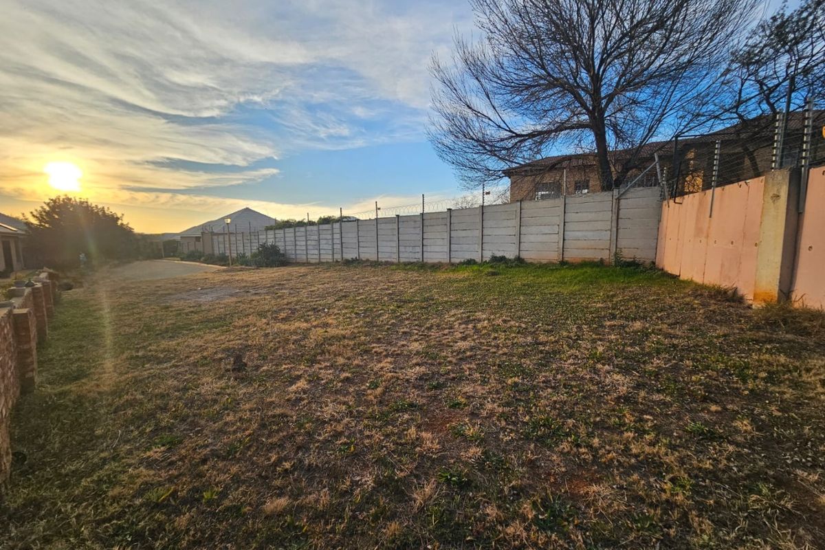 A vacant residential plot featuring a precast concrete boundary wall with electric fencing, set against a sunset backdrop.